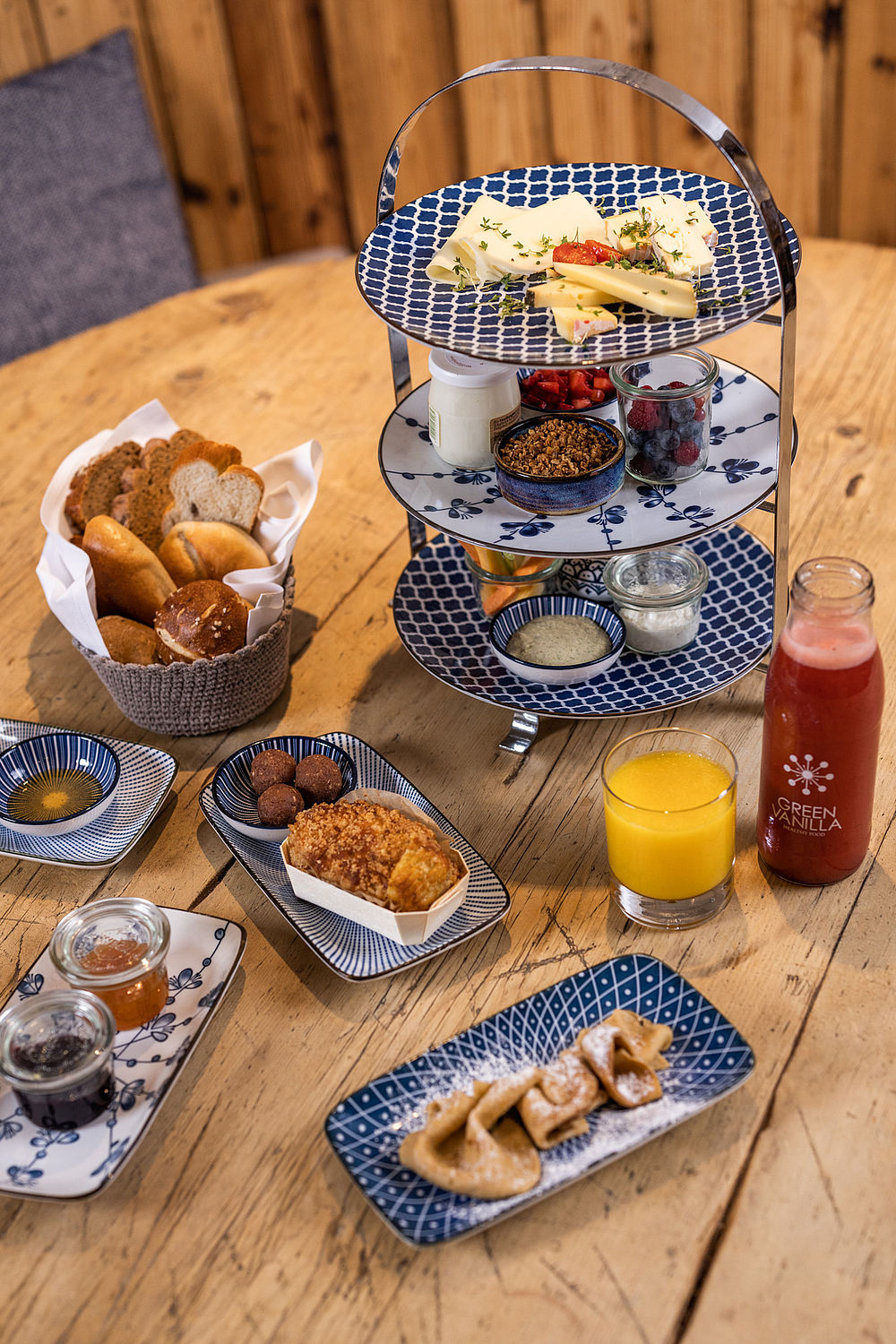 Breakfast table with fresh juices, a cake stand with different types of cheese, muesli, fresh fruit and various baked goods