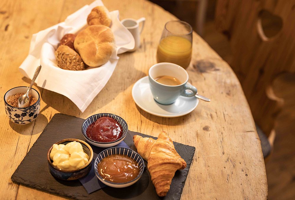 Ein Frühstück mit Cafe, frischem Croissant, Brot und Marmelade und Orangensaft
