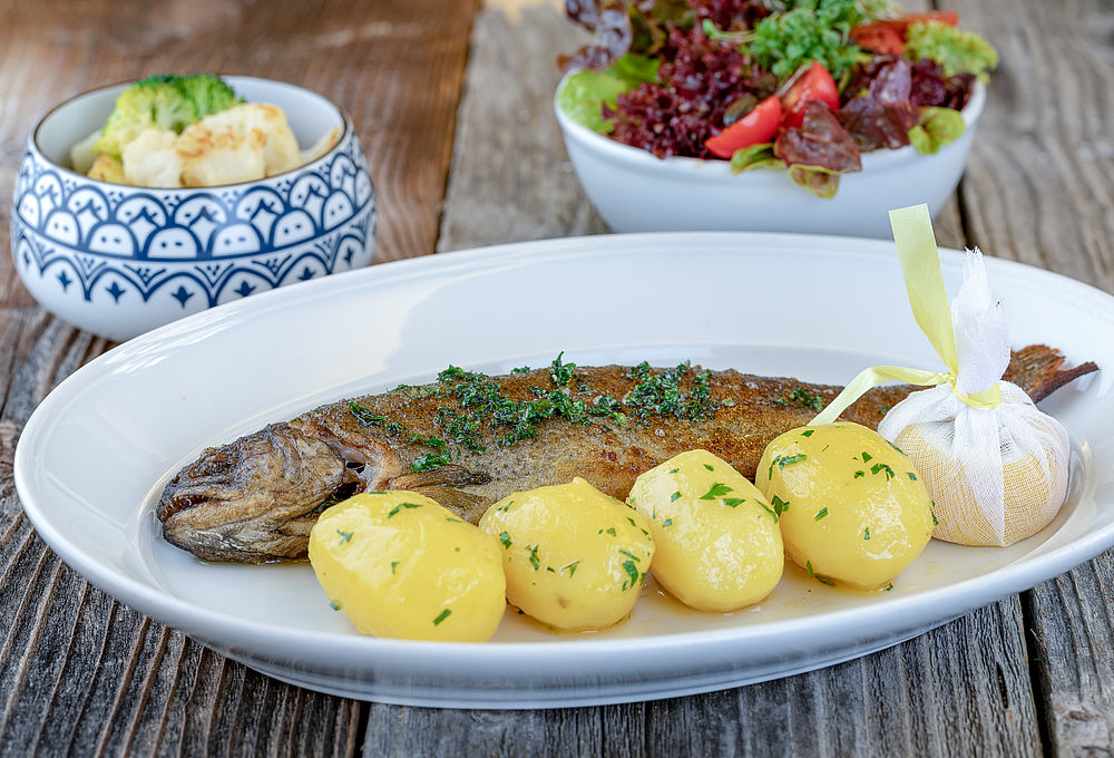Un pesce fritto croccante viene servito su un piatto con guarnizioni fresche al Gasthof Goldgasse