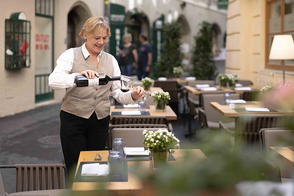 Una cameriera versa il vino in un bicchiere sulla terrazza del Gasthof Goldgasse